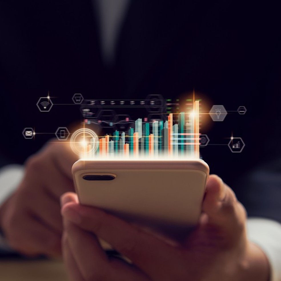 Stock exchange market concept, hand trader holding smartphone with graphs analysis candle line on bokeh colors light in night. (Foto: Getty Images/iStockphoto) — Foto: Glamour