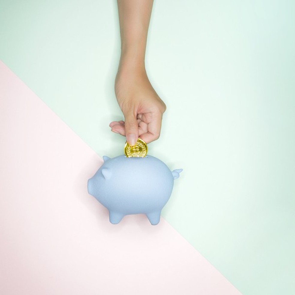 Hand reaching out to piggy bank on pastel colour background. (Foto: Getty Images) — Foto: Glamour