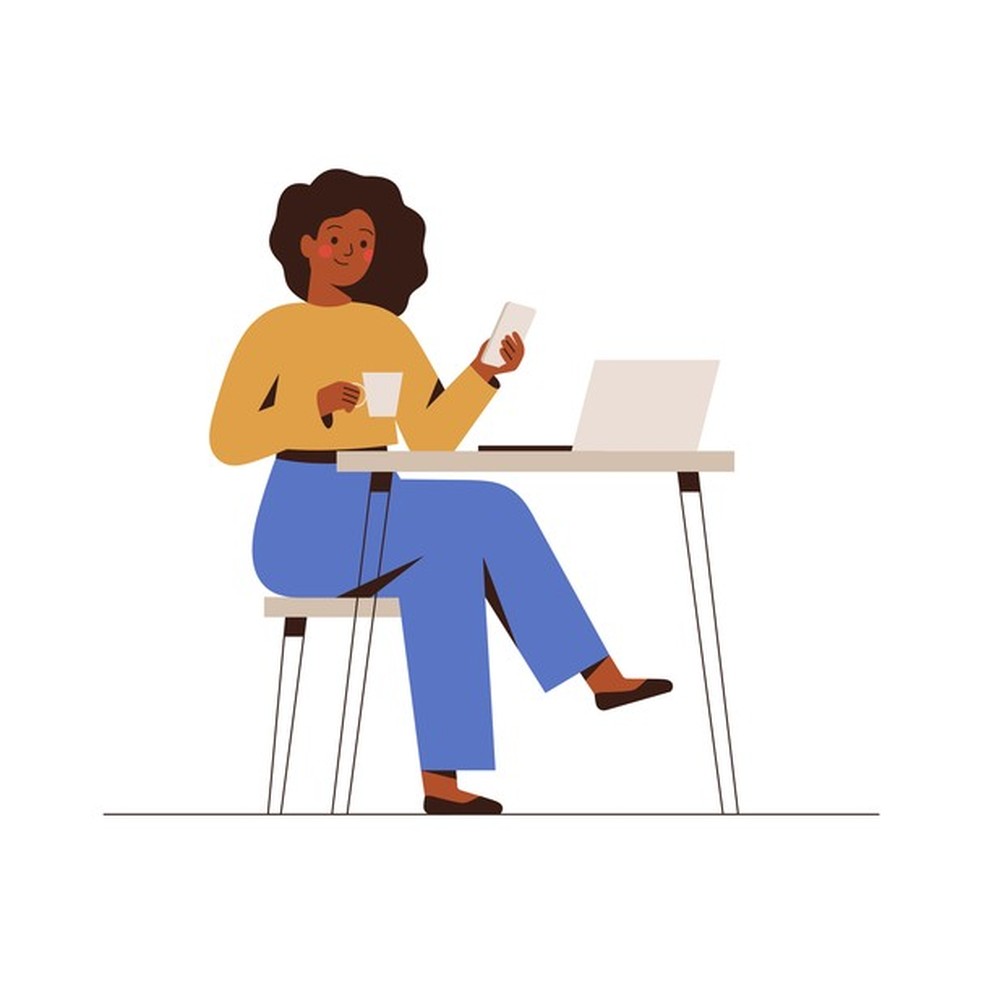 Black Woman chatting on a smartphone sitting at the cafe table. Happy freelancer or office female working remotely use a laptop. African girl looking at the phone, drinking coffee at the workplace. (Foto: Getty Images/iStockphoto) — Foto: Glamour