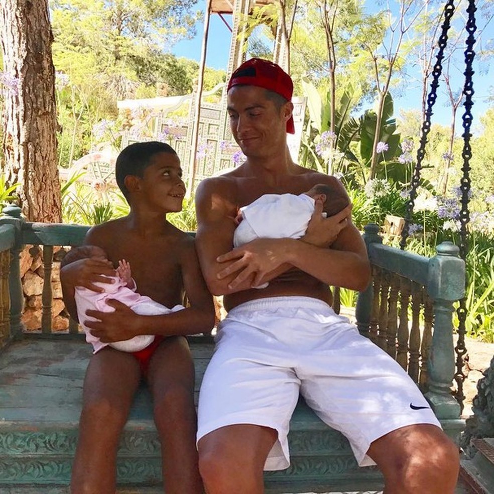 Está vendo os gêmeos fofinhos no colo de Cristiano Ronaldo e seu filho mais velho? Eles nasceram de barriga de aluguel (Foto: Instagram/Reprodução) — Foto: Glamour