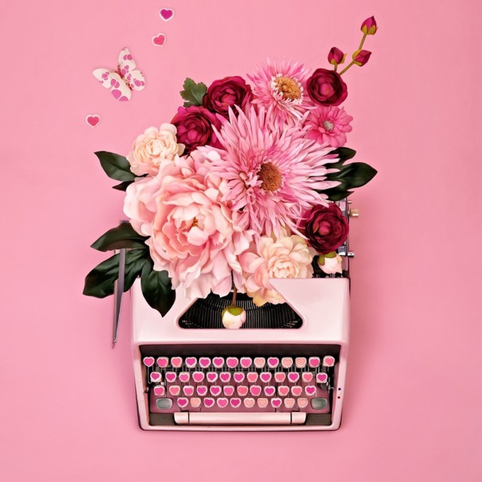 Vintage typewriter with candy heart keys and filled with a flower arrangement on a pink background (Foto: Getty Images) — Foto: Glamour