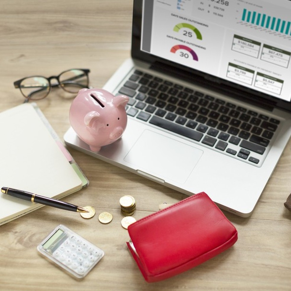 Piggy bank, laptop, purse with money, coffee cup on wooden table top. (Foto: Getty Images) — Foto: Glamour