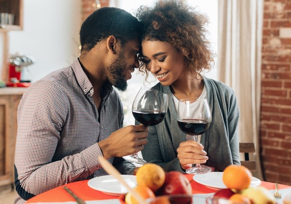 African-american couple enjoying romantic dinner at home, cheering with glasses of red wine (Foto: Getty Images/iStockphoto) — Foto: Glamour
