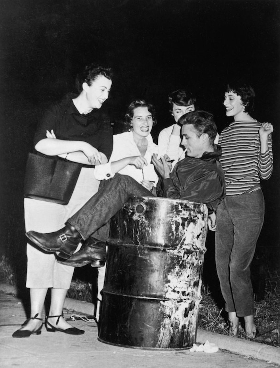 O ator James Dean dando autógrafo para fãs sentado em um latão de lixo é a cara da rebeldia da época. Claro que ele estava de jeans (Foto: Getty Images) — Foto: Glamour